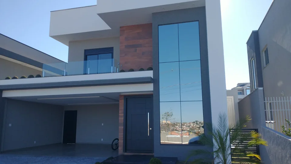 Fachada residencial com pano de vidro refletivo e esquadrias escuras.